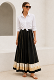 Woman wearing a black cotton rayon flared maxi skirt with woven gold brocade border and pleated silhouette by Tjori