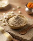 Bowl filled with Multani mitti and rose face pack powder on a stone slab with wooden spatula